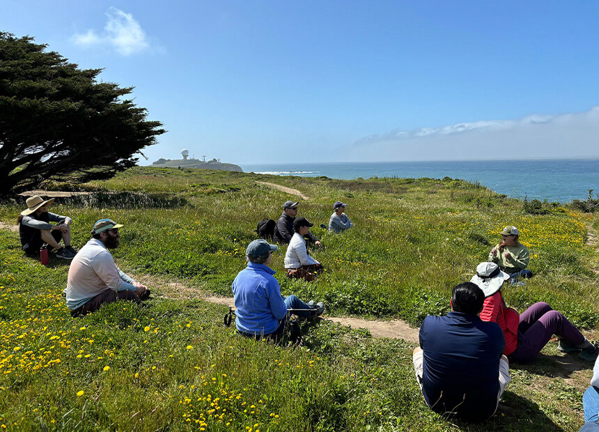 Docents and participants sitting in grass overlooking the ocea